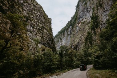 Dağların arasındaki yol. Önünde siyah bir SUV var.