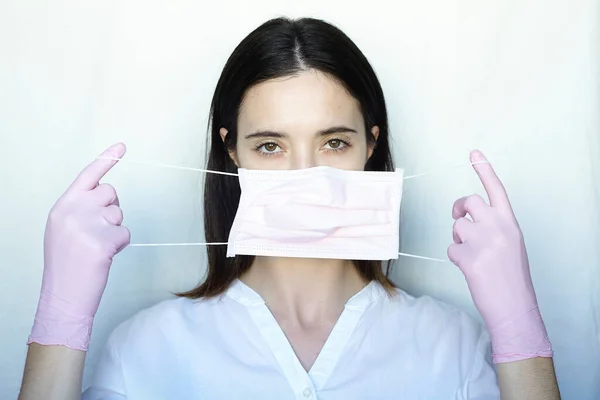 Pembe eldivenli bir kadın pembe koruyucu bir maske takıyor. Kız beyaz elbiseli hafif bir arka planda duruyor. Coronavirüs 'ün bastırılması kavramı