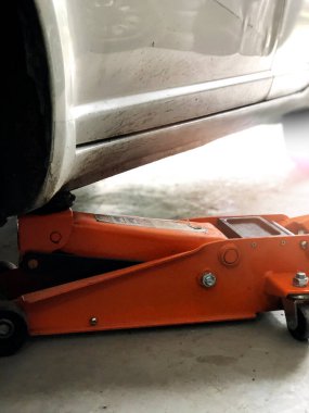 Adam direksiyon değiştirmek için kriko kullanarak araba kaldırıyor. Kış ve yaz lastikleri değiştiriliyor. Mevsimlik lastik değiştirme kavramı