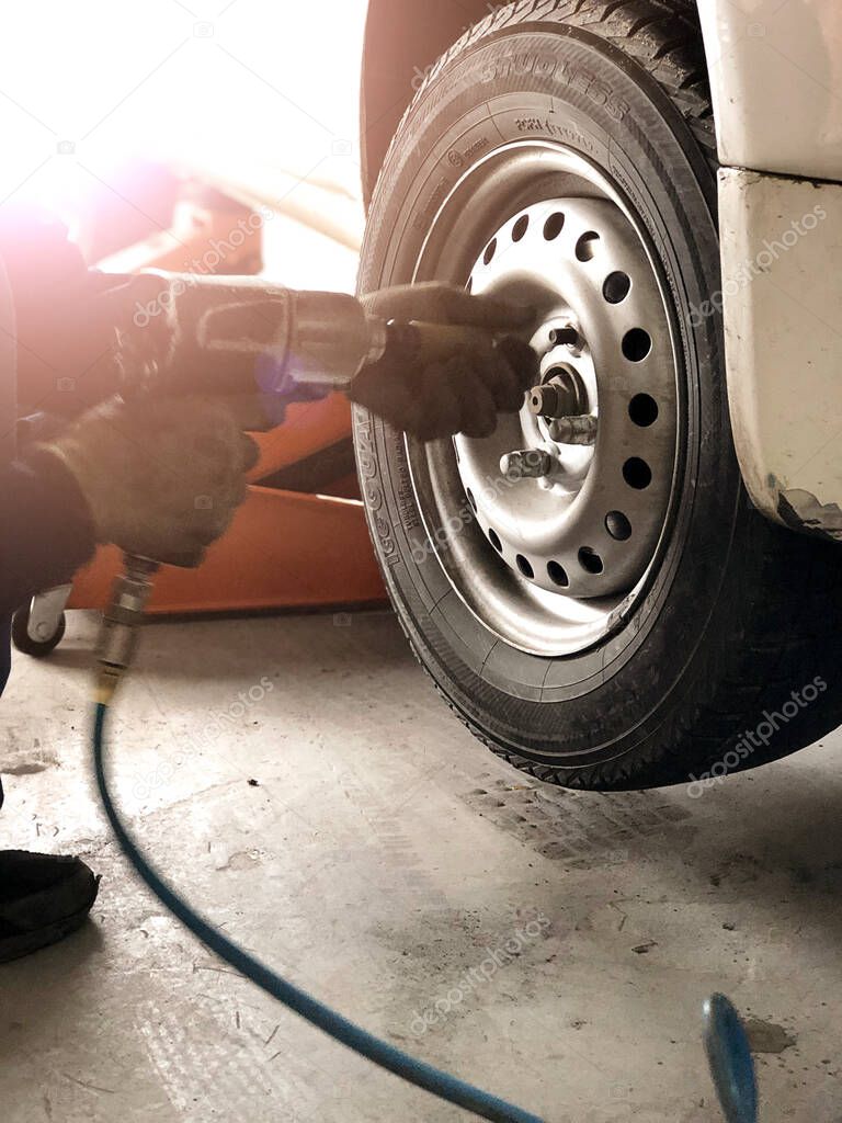 Auto mechanic man with electric screwdriver changing tire outside. Car service.  Tire installation concept. Replacement of winter and summer tires. Hands replace tires on wheels.