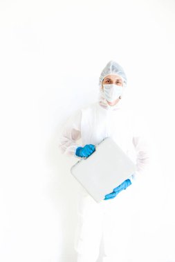 Koruyucu takım elbiseli, eldivenli ve maskeli bir adam elinde bir bavulla elinde testler için yürüyor. Koronavirüsle mücadele kavramı. Beyaz bir arkaplanda izole edilmiş