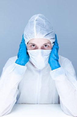 Koruyucu giysili, eldivenli ve maskeli bir adam kafasında panik ya da korku taklidi yapıyor. Sağlık kavramı.
