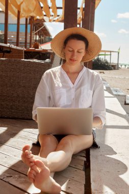 Kumsalda dizüstü bilgisayar kullanan genç bir kadın. Serbest çalışma kavramı