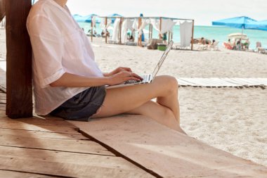 Kumsalda dizüstü bilgisayar kullanan genç bir kadın. Serbest çalışma kavramı