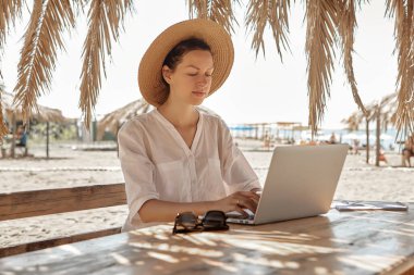 Kumsalda dizüstü bilgisayar kullanan genç bir kadın. Serbest çalışma kavramı
