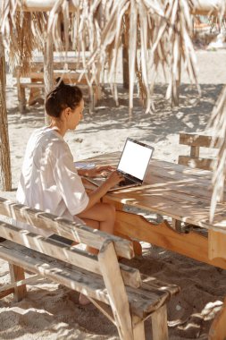 Kumsalda dizüstü bilgisayar kullanan genç bir kadın. Serbest çalışma kavramı