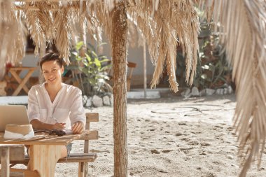 Kumsalda dizüstü bilgisayar kullanan genç bir kadın. Serbest çalışma kavramı