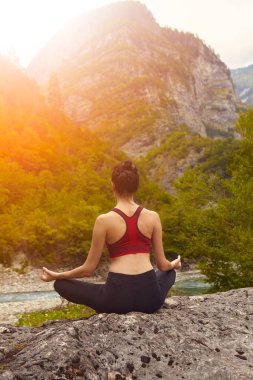 Doğada yoga dersleri. Tek başına spor yapma kavramı. Sosyal dışlama. Bir kadın kayalıklarda yoga yapıyor, bir dağ nehrinin yanında.