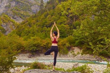 Doğada yoga dersleri. Tek başına spor yapma kavramı. Sosyal dışlama. Bir kadın kayalıklarda yoga yapıyor, bir dağ nehrinin yanında.