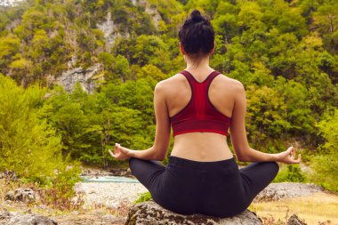 Doğada yoga dersleri. Tek başına spor yapma kavramı. Sosyal dışlama. Bir kadın kayalıklarda yoga yapıyor, bir dağ nehrinin yanında.
