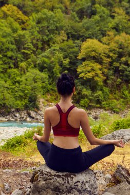 Doğada yoga dersleri. Tek başına spor yapma kavramı. Sosyal dışlama. Bir kadın kayalıklarda yoga yapıyor, bir dağ nehrinin yanında.