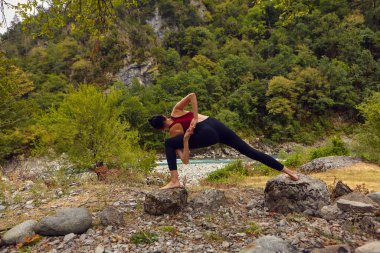 Doğada yoga dersleri. Tek başına spor yapma kavramı. Sosyal dışlama. Bir kadın kayalıklarda yoga yapıyor, bir dağ nehrinin yanında.