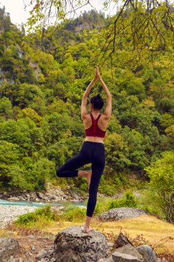 Doğada yoga dersleri. Tek başına spor yapma kavramı. Sosyal dışlama. Bir kadın kayalıklarda yoga yapıyor, bir dağ nehrinin yanında.