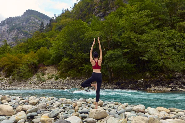 Yoga classes in nature. The concept of playing sports alone. Social exclusion. A woman does yoga on rocks, near a mountain river flows