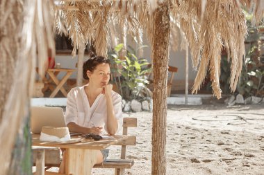 Kumsalda dizüstü bilgisayar kullanan genç bir kadın. Serbest çalışma kavramı