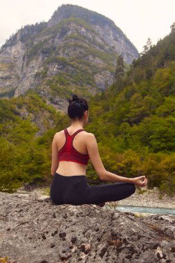 Doğada yoga dersleri. Tek başına spor yapma kavramı. Sosyal dışlama. Bir kadın kayalıklarda yoga yapıyor, bir dağ nehrinin yanında.