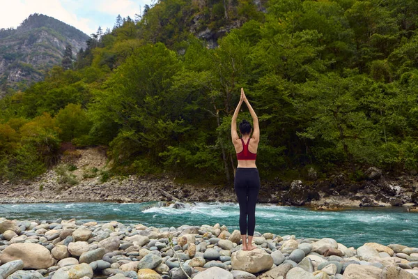 Yoga classes in nature. The concept of playing sports alone. Social exclusion. A woman does yoga on rocks, near a mountain river flows