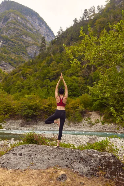 Yoga classes in nature. The concept of playing sports alone. Social exclusion. A woman does yoga on rocks, near a mountain river flows