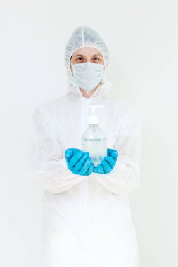 Koruyucu kıyafetli bir adam el dezenfeksiyonu için antibakteriyel antiseptik jel tutuyor. Grip salgını ve koronavirüs salgını sırasında sağlık hizmetlerinin önlenmesi
