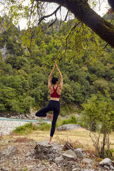 Doğada yoga dersleri. Tek başına spor yapma kavramı. Sosyal dışlama. Bir kadın kayalıklarda yoga yapıyor, bir dağ nehrinin yanında.