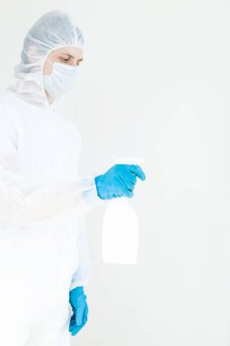 Koruyucu giysili eldiven ve maske takmış elinde sprey tutan bir adam. Antibakteriyel tedavi kavramı. Beyaz bir arkaplanda izole edilmiş
