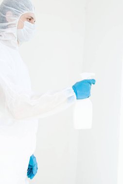 Koruyucu giysili eldiven ve maske takmış elinde sprey tutan bir adam. Antibakteriyel tedavi kavramı. Beyaz bir arkaplanda izole edilmiş