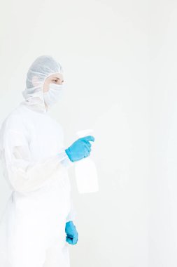 Koruyucu giysili eldiven ve maske takmış elinde sprey tutan bir adam. Antibakteriyel tedavi kavramı. Beyaz bir arkaplanda izole edilmiş