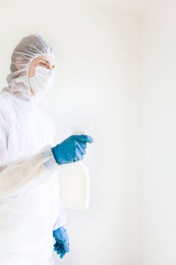 Koruyucu giysili eldiven ve maske takmış elinde sprey tutan bir adam. Antibakteriyel tedavi kavramı. Beyaz bir arkaplanda izole edilmiş