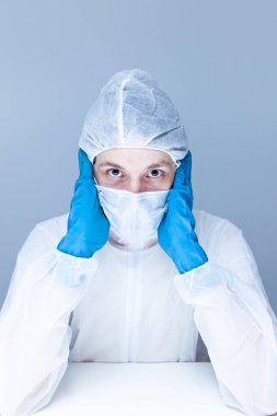 Koruyucu giysili, eldivenli ve maskeli bir adam kafasında panik ya da korku taklidi yapıyor. Sağlık kavramı.