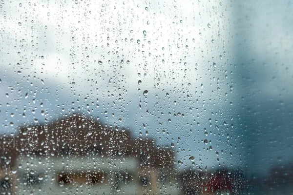Close up of a window with rain drops falling down. Focus on rain drops. Rain drops on rainy day on outside window glass with blurred edges. Rain outside window pane in spring day.