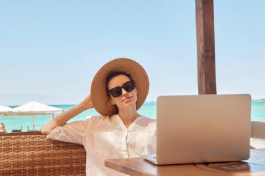 Kumsalda dizüstü bilgisayar kullanan genç bir kadın. Serbest çalışma kavramı