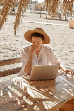 Kumsalda dizüstü bilgisayar kullanan genç bir kadın. Serbest çalışma kavramı