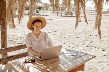 Kumsalda dizüstü bilgisayar kullanan genç bir kadın. Serbest çalışma kavramı