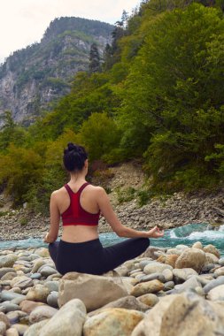 Doğada yoga dersleri. Tek başına spor yapma kavramı. Sosyal dışlama. Bir kadın kayalıklarda yoga yapıyor, bir dağ nehrinin yanında.