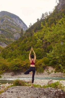 Doğada yoga dersleri. Tek başına spor yapma kavramı. Sosyal dışlama. Bir kadın kayalıklarda yoga yapıyor, bir dağ nehrinin yanında.