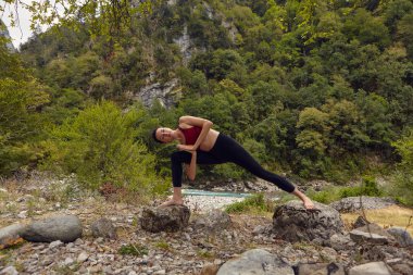 Doğada yoga dersleri. Tek başına spor yapma kavramı. Sosyal dışlama. Bir kadın kayalıklarda yoga yapıyor, bir dağ nehrinin yanında.