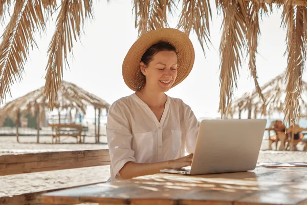 Kumsalda dizüstü bilgisayar kullanan genç bir kadın. Serbest çalışma kavramı