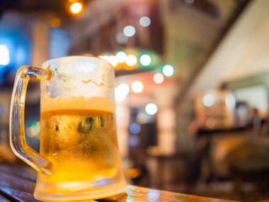 Bir restoranın arka planındaki ahşap masanın üzerine bira bardağını kapat, gece lambası fotokopi alanı