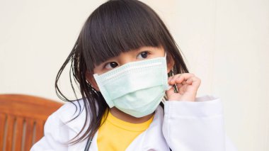 Oyuncu küçük kız doktorculuk oynuyor, evde eğleniyor, tatlı kız hemşire rolü yapıyor, beyaz arka planda tıbbi maske takıyor.