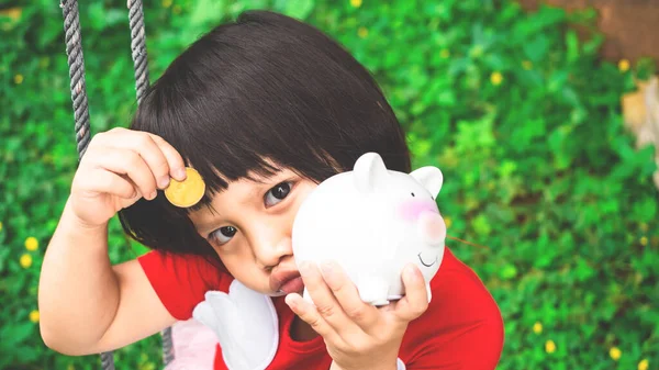 adorable 3 years old child holding coins and piggy bank in hand, saving money for dream, future and education for children concept.