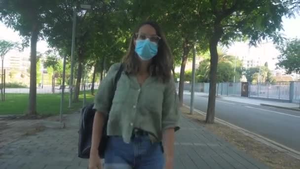 若いです女の子見ながら彼女の携帯電話とともに歩くとコロナウイルスマスク — ストック動画
