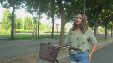 Gözlüklü genç kız cep telefonuna bakıyor ve elinde bir bisiklet tutuyor.