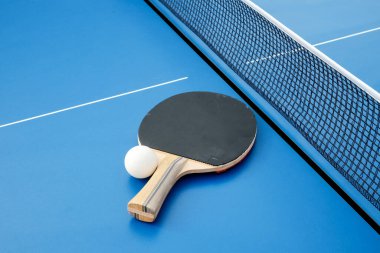 Masa tenisi için siyah ahşap raket ve ağın yanındaki mavi masada duran beyaz top..