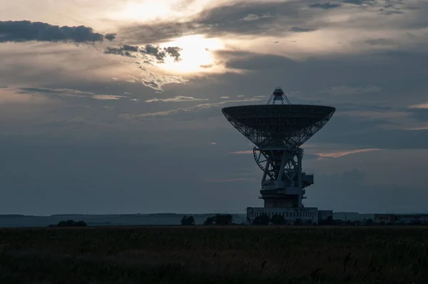 Space radar antenna. Satellite dish at sunset with cloudy sky.