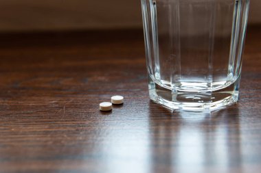 Haplar, ahşap bir masanın üzerinde, bir bardak suyun yanında yatıyor..