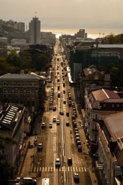 Gün batımında güneşli bir günde araba siluetleri ve yayalar olan uzun Central City caddesinin manzarası. Üst görünüm dikey.