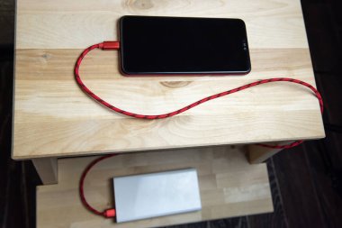 Akıllı telefon tahtadan sandalyede güç bankasıyla şarj oluyor..