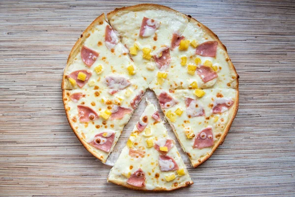 Hawaiian pizza with pineapple, sliced slice of pizza on a wooden background top view.