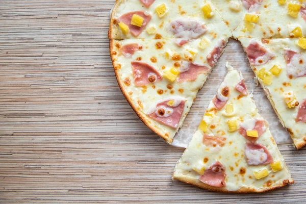 Sliced slice of hawaiian pizza on a wooden background top view with copy space.