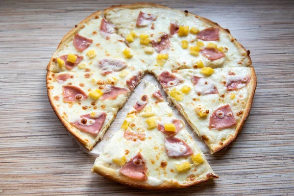 Hawaiian pizza with pineapple, sliced slice of pizza on a wooden background close up.